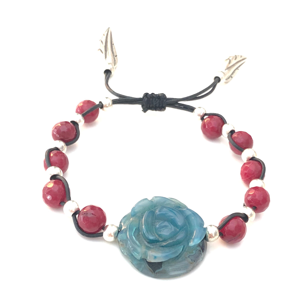 Elegante pulsera ajustable de ágata facetada borgoña entrelazadas con las de zamak con baño de plata. El centro de atención de la pieza es la espectacular rosa de ágata turquesa que junto con los terminales de pluma de Zamak con baño de plata permiten combinarla con tus prendas de diario.